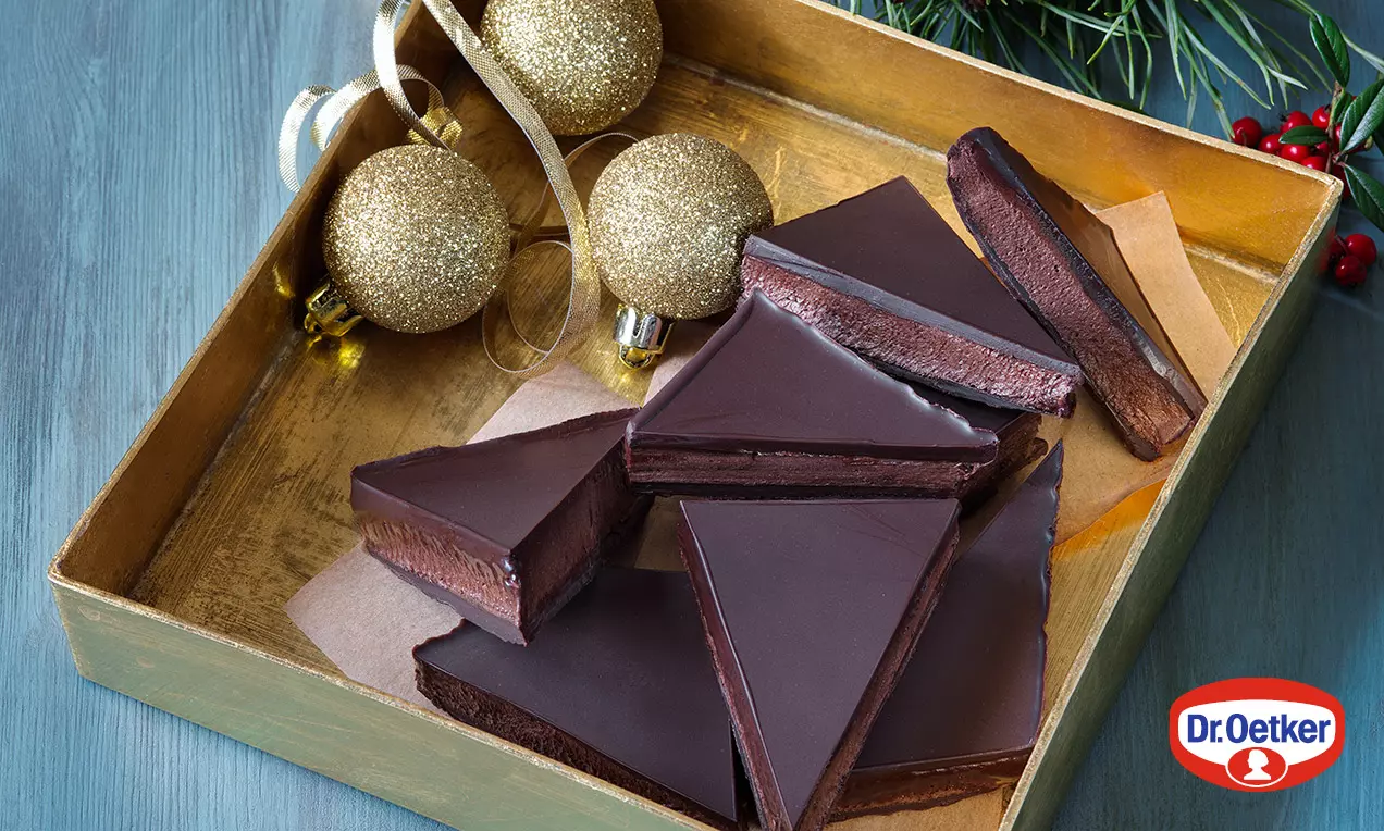 Čokoládové trojúhelníčky s hladkým tmavým povrchem a čokoládovou vrstvou na papíře ve zlaté krabičce, dekorované třpytivými koulemi s větvičkou