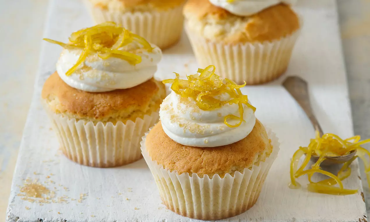 Cupcakes ve světlém papírovém košíčku, se svěží citronovou kůrou na nadýchaném krému, uspořádané na bílé dřevěné desce