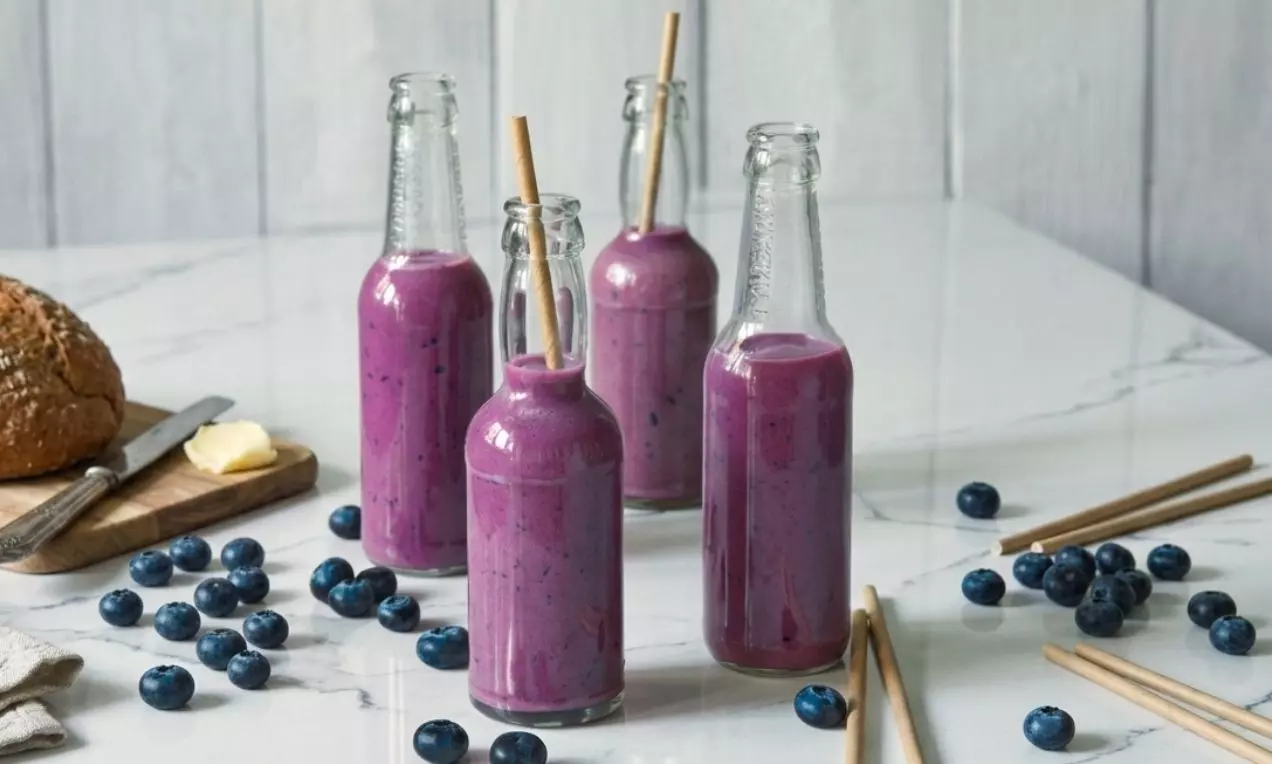 Štíhlé skleněné lahve s hustým fialovým smoothie, doplněné bambusovými brčky, obklopené čerstvými borůvkami na mramorovém stole, AI-labeled image