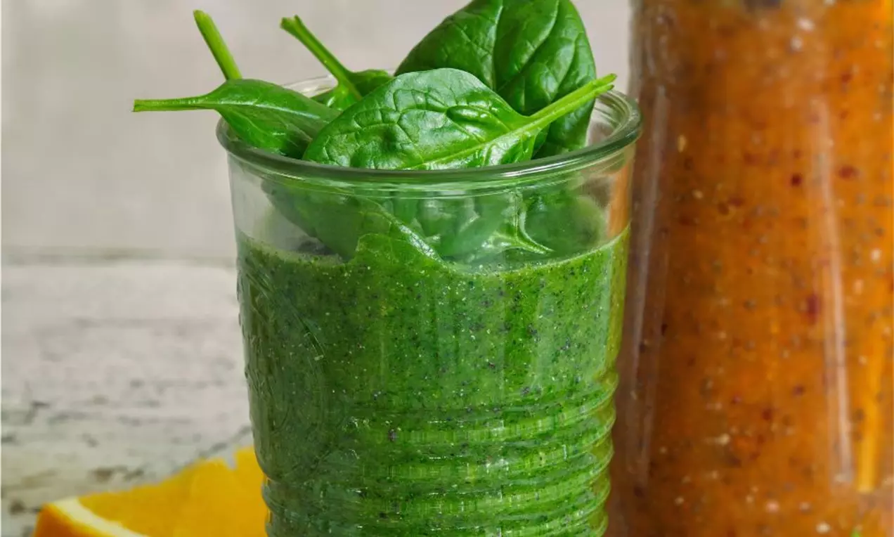 Makové smoothie v průhledné sklenici, husté a tmavě zelené, s hladkým povrchem, zdobené čerstvými listy špenátu, na světlém stole